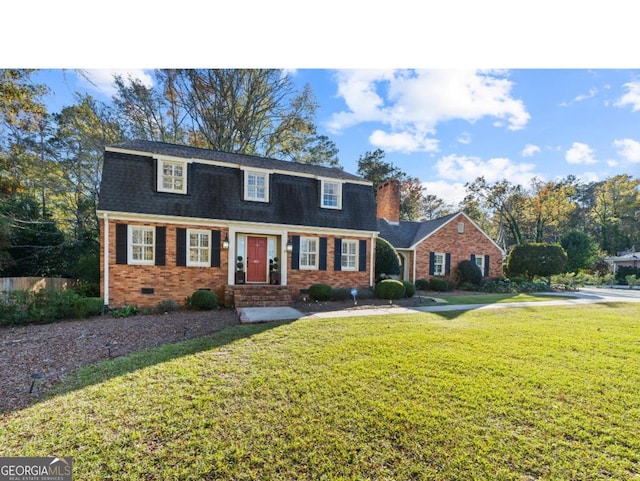 dutch colonial with entry steps, brick siding, roof with shingles, a chimney, and a front yard