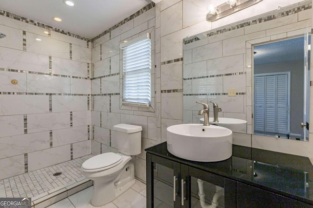 bathroom with tiled shower, vanity, toilet, and tile walls