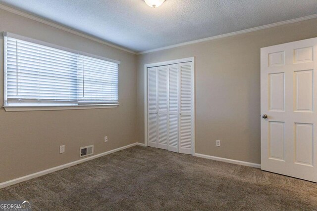 unfurnished bedroom featuring carpet, a textured ceiling, a closet, and crown molding