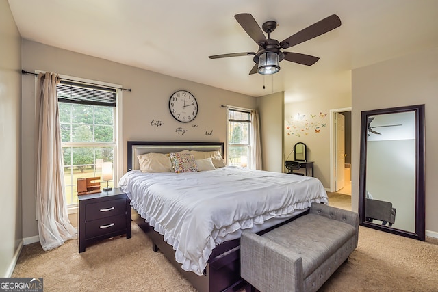 carpeted bedroom featuring ensuite bath, multiple windows, and ceiling fan