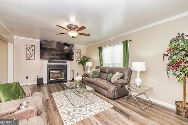 living room featuring hardwood / wood-style floors, ceiling fan, crown molding, and a tiled fireplace