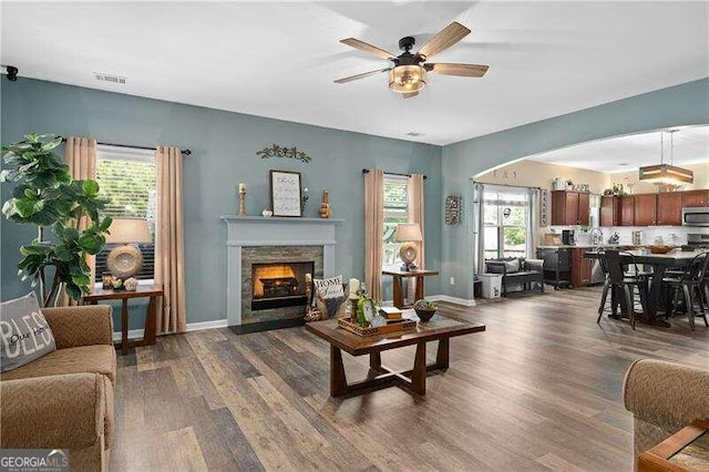 living room featuring a stone fireplace, ceiling fan, and dark hardwood / wood-style floors