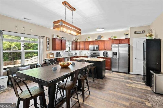 kitchen featuring a kitchen bar, stainless steel appliances, decorative light fixtures, an inviting chandelier, and hardwood / wood-style flooring