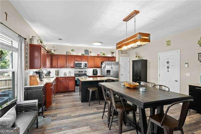 kitchen with hanging light fixtures, a kitchen breakfast bar, dark hardwood / wood-style flooring, a kitchen island, and appliances with stainless steel finishes