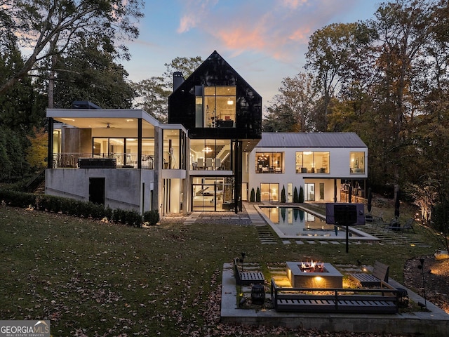 back house at dusk with ceiling fan, a balcony, a yard, a patio, and an outdoor fire pit