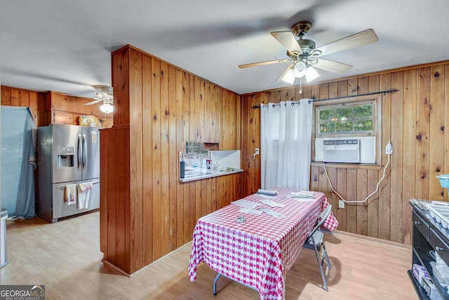 kitchen with ceiling fan, stainless steel refrigerator with ice dispenser, wooden walls, and light hardwood / wood-style flooring