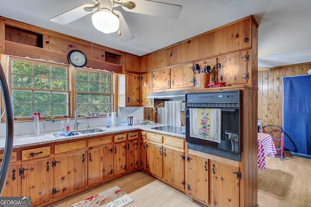 kitchen with black appliances, sink, wooden walls, light hardwood / wood-style floors, and light stone counters