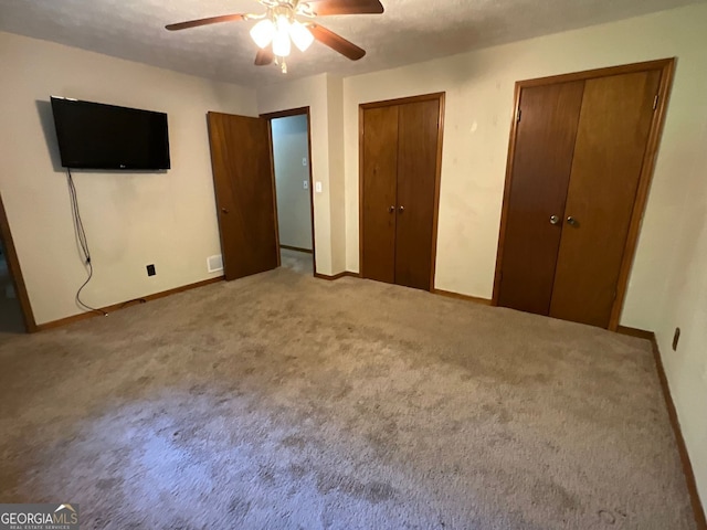 unfurnished bedroom featuring ceiling fan, two closets, a textured ceiling, and light carpet