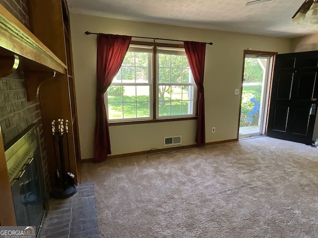 unfurnished living room featuring carpet floors, ceiling fan, a fireplace, and a textured ceiling