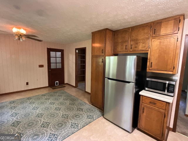 kitchen featuring wood walls, a textured ceiling, stainless steel appliances, and ceiling fan