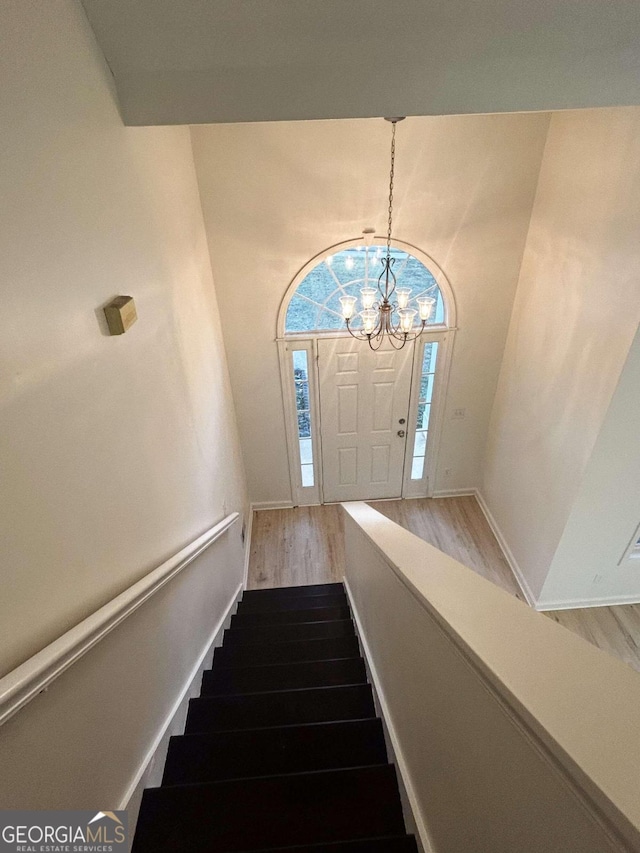 stairway with wood-type flooring and an inviting chandelier