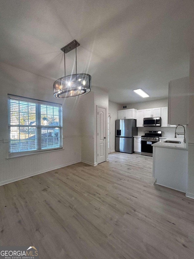 kitchen with pendant lighting, white cabinets, sink, light wood-type flooring, and appliances with stainless steel finishes