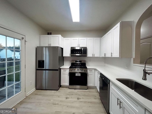 kitchen featuring light wood-type flooring, stainless steel appliances, sink, a water view, and white cabinets