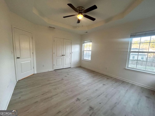 unfurnished bedroom featuring a tray ceiling, ceiling fan, and light hardwood / wood-style floors