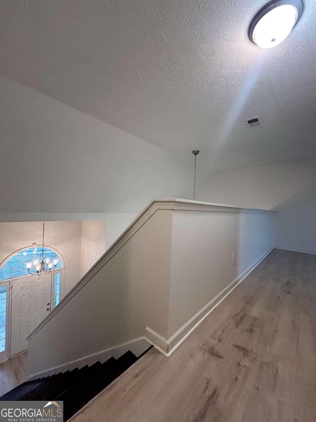 stairway featuring a chandelier, hardwood / wood-style floors, a textured ceiling, and vaulted ceiling