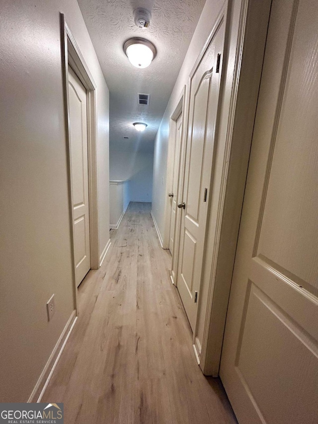 corridor featuring a textured ceiling and light hardwood / wood-style flooring