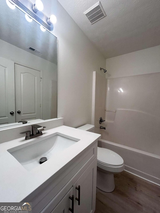 full bathroom featuring hardwood / wood-style floors, vanity, shower / washtub combination, toilet, and a textured ceiling