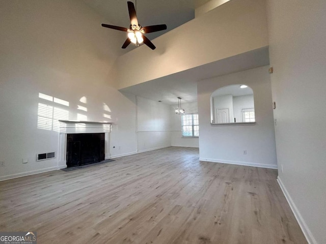 unfurnished living room featuring a towering ceiling, light hardwood / wood-style floors, and ceiling fan