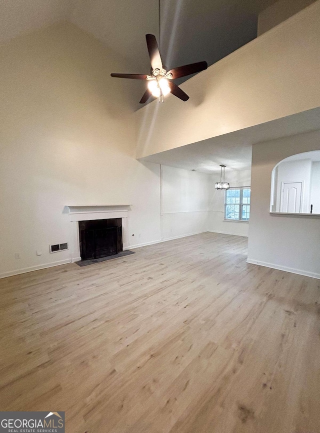 unfurnished living room featuring ceiling fan with notable chandelier, light wood-type flooring, and high vaulted ceiling