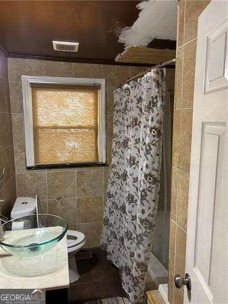 bathroom with curtained shower, tile walls, and toilet