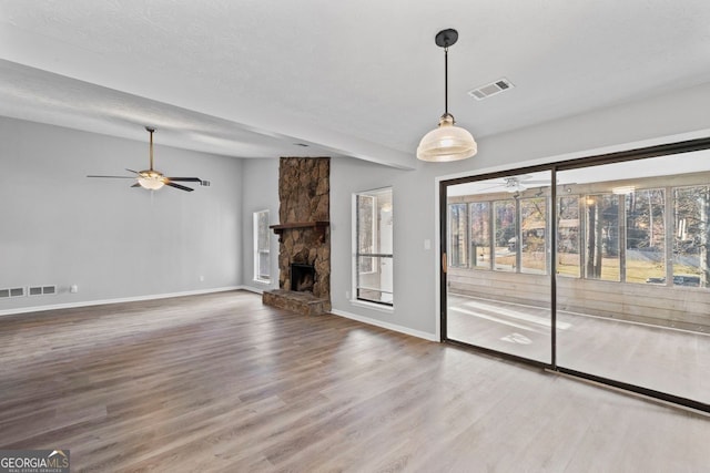 unfurnished living room with hardwood / wood-style flooring, a stone fireplace, and a textured ceiling