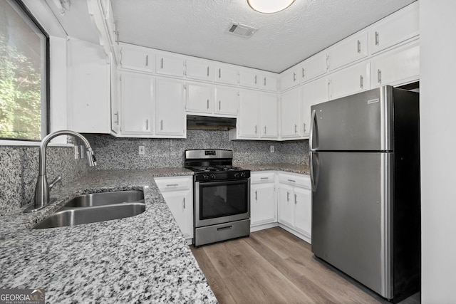 kitchen with light stone countertops, a textured ceiling, stainless steel appliances, sink, and white cabinets