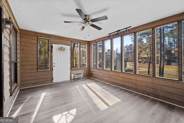 unfurnished sunroom with a wall mounted air conditioner, ceiling fan, and a healthy amount of sunlight