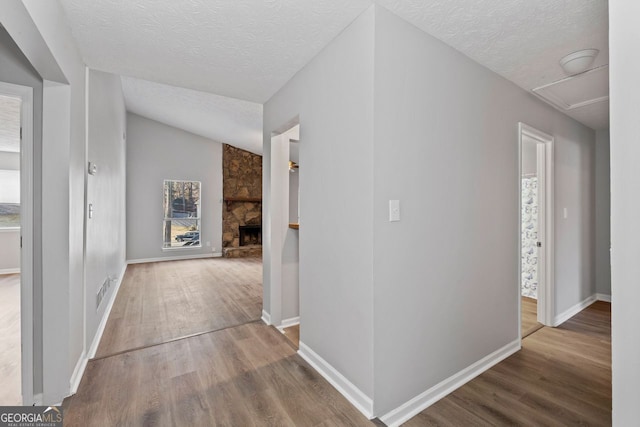 corridor with vaulted ceiling, hardwood / wood-style floors, and a textured ceiling