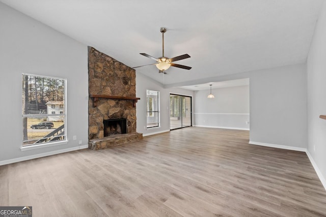 unfurnished living room with a stone fireplace, a wealth of natural light, ceiling fan, and hardwood / wood-style flooring