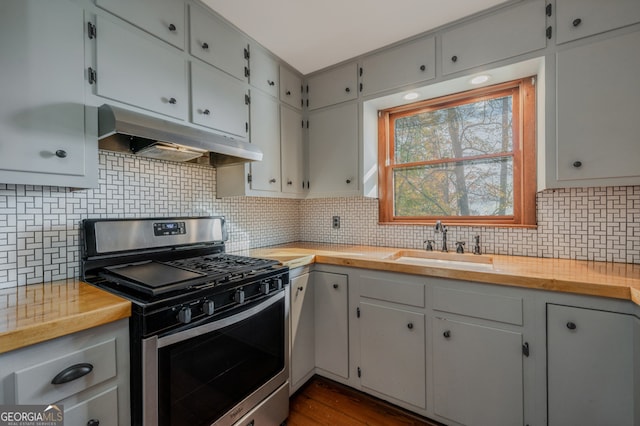 kitchen with decorative backsplash, wood counters, stainless steel gas range oven, dark wood-type flooring, and sink