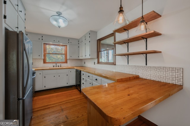 kitchen with stainless steel refrigerator, white cabinetry, light hardwood / wood-style flooring, kitchen peninsula, and pendant lighting