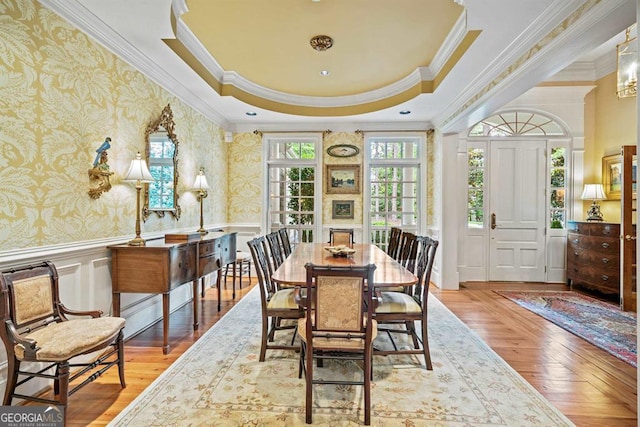 dining space with a raised ceiling, light wood-type flooring, and ornamental molding