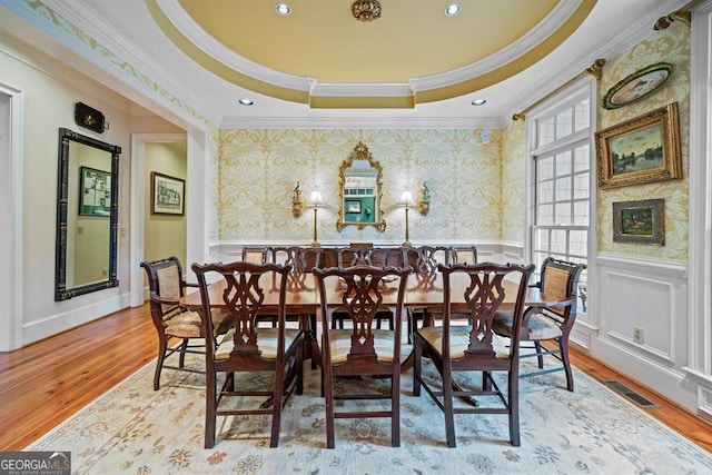 dining space with light wood-type flooring, a tray ceiling, and ornamental molding