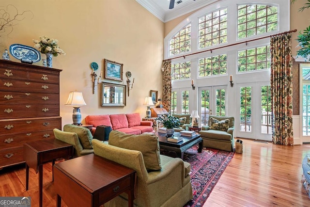 living room featuring light hardwood / wood-style floors, a towering ceiling, crown molding, and french doors