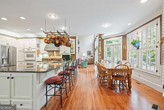 kitchen with stainless steel fridge, crown molding, dark stone counters, white cabinets, and light wood-type flooring