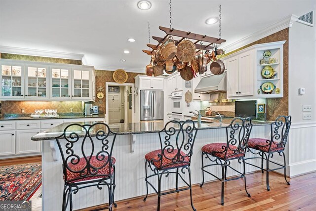 kitchen featuring white cabinetry, white oven, light hardwood / wood-style flooring, stainless steel refrigerator with ice dispenser, and kitchen peninsula