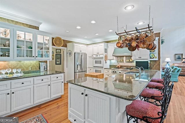 kitchen featuring dark stone counters, crown molding, stainless steel refrigerator with ice dispenser, light hardwood / wood-style flooring, and a kitchen bar