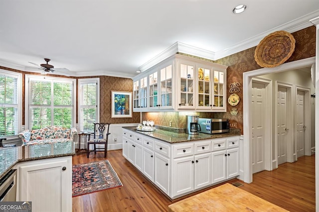 kitchen with appliances with stainless steel finishes, light hardwood / wood-style flooring, white cabinetry, and dark stone counters