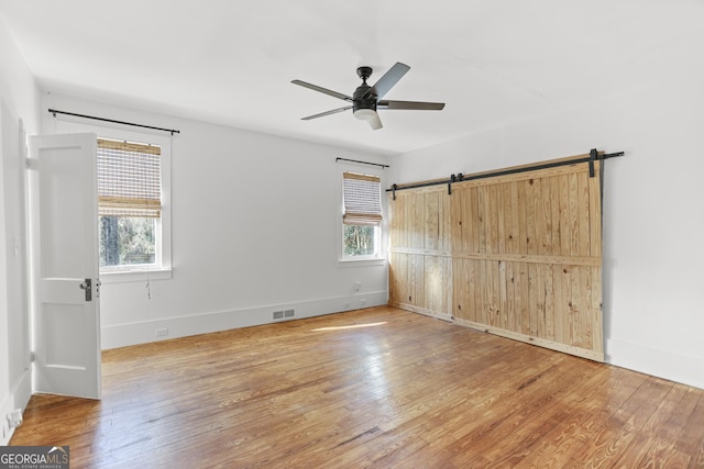 unfurnished bedroom with hardwood / wood-style floors, a barn door, and ceiling fan