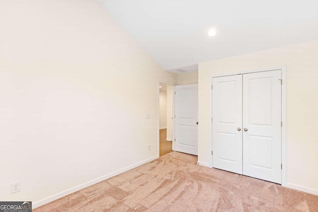 unfurnished bedroom featuring light carpet, vaulted ceiling, and a closet