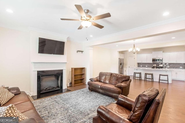 living room with ceiling fan with notable chandelier, ornamental molding, and light hardwood / wood-style flooring