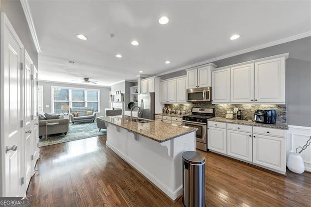 kitchen with a kitchen island with sink, dark hardwood / wood-style floors, a kitchen bar, white cabinetry, and stainless steel appliances