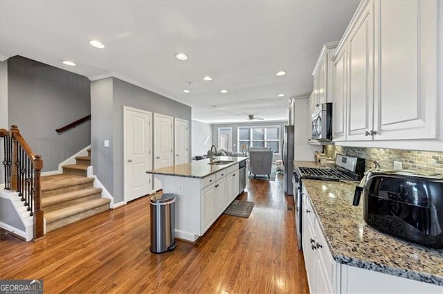 kitchen featuring a center island with sink, white cabinets, hardwood / wood-style floors, and appliances with stainless steel finishes