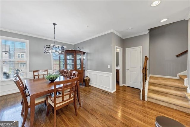 dining area with hardwood / wood-style floors, crown molding, and an inviting chandelier