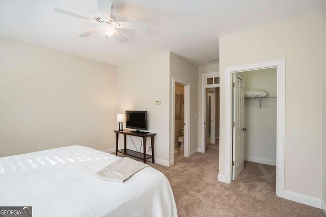 carpeted bedroom featuring connected bathroom, a walk in closet, ceiling fan, and a closet