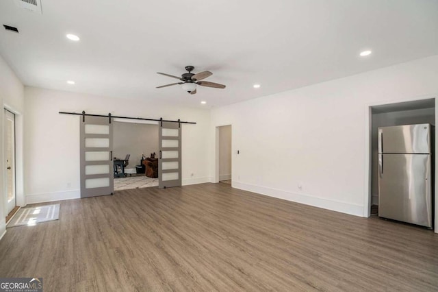 unfurnished living room featuring wood-type flooring, a barn door, and ceiling fan