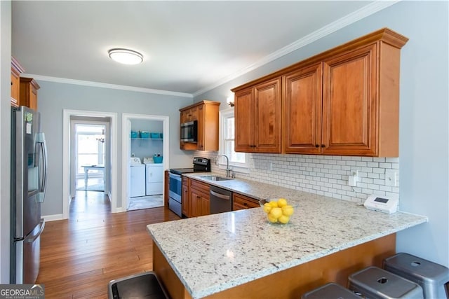 kitchen featuring sink, a kitchen bar, kitchen peninsula, stainless steel appliances, and washer and clothes dryer