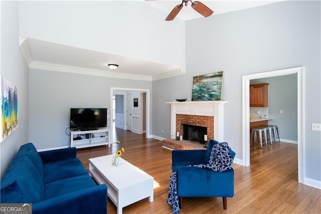 living room featuring ceiling fan, wood-type flooring, ornamental molding, and a brick fireplace