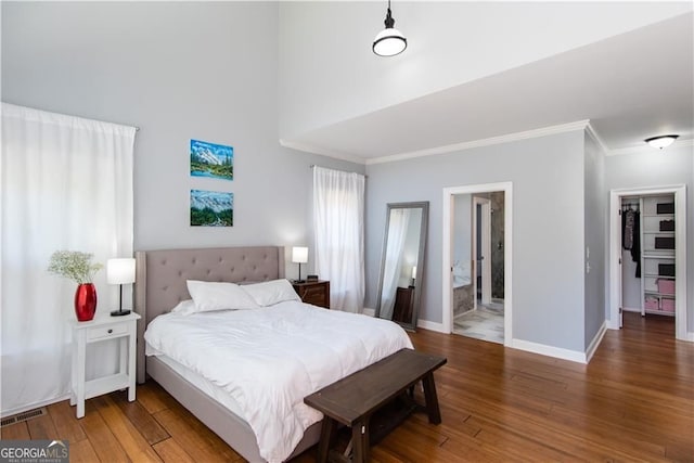 bedroom with wood-type flooring, a walk in closet, ensuite bath, and crown molding