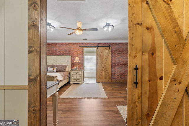 bedroom featuring a barn door, crown molding, dark hardwood / wood-style flooring, and brick wall